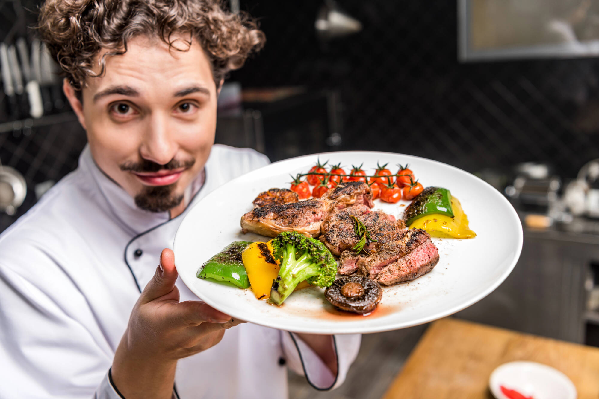 A chef holding a plate of tasty cooked meat and vegetables
